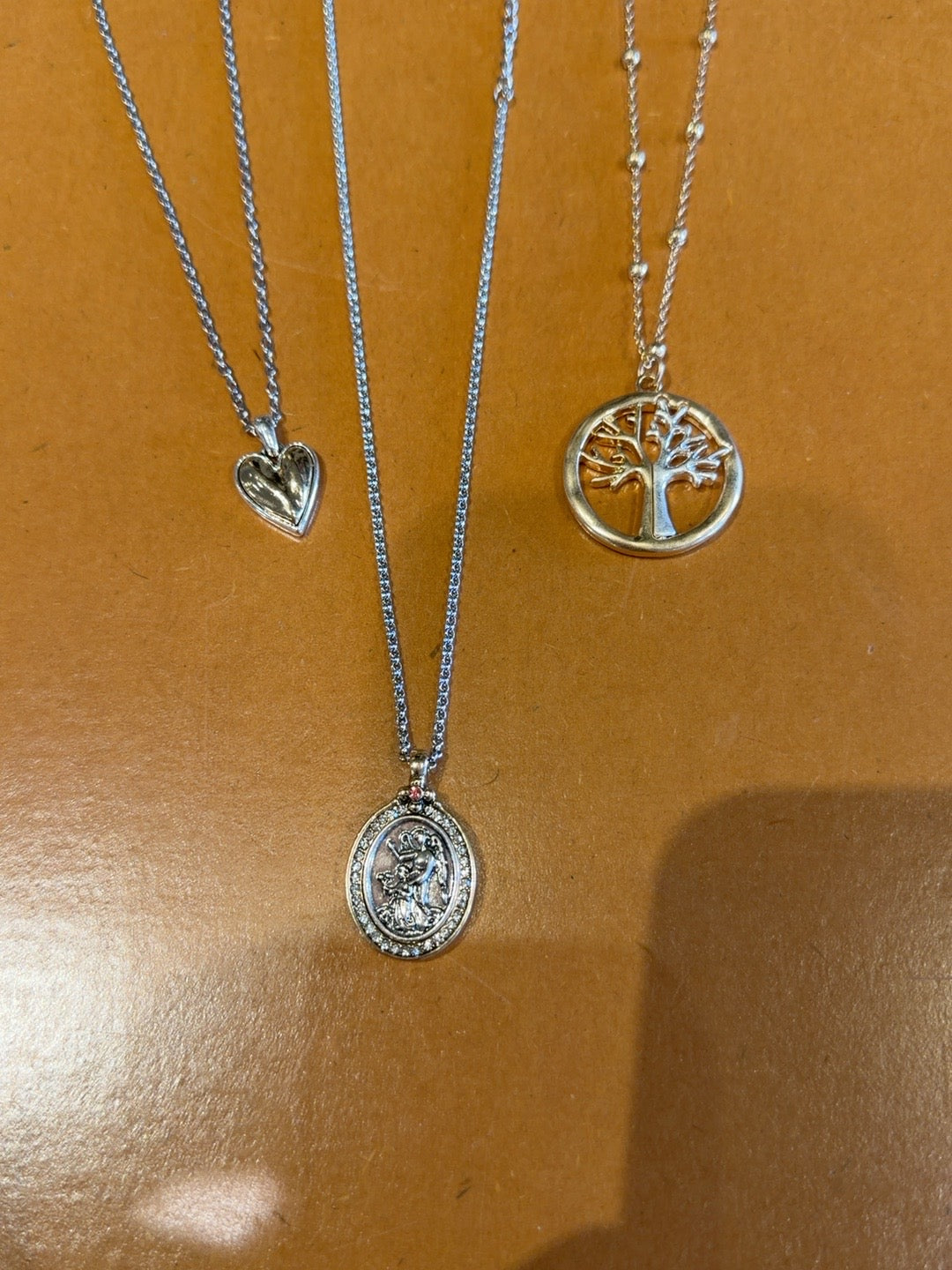 Three necklaces with heart, tree of life and saint medallion pendants