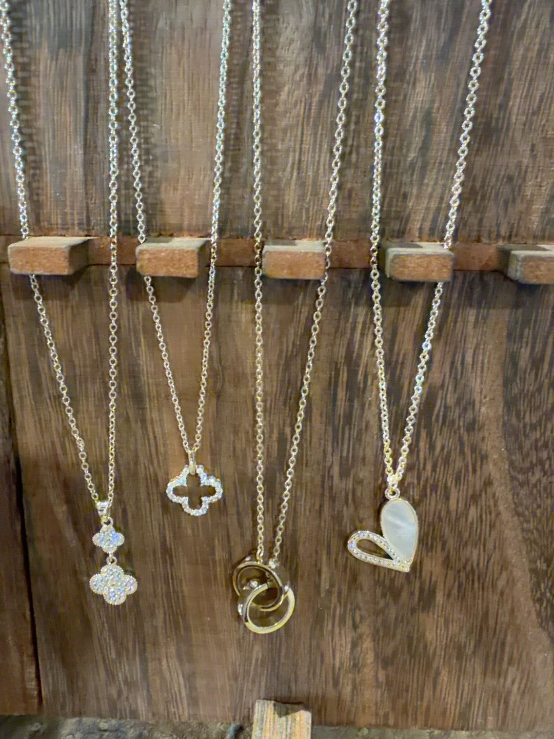Four gold-tone necklaces featuring clover, linked rings and heart pendants