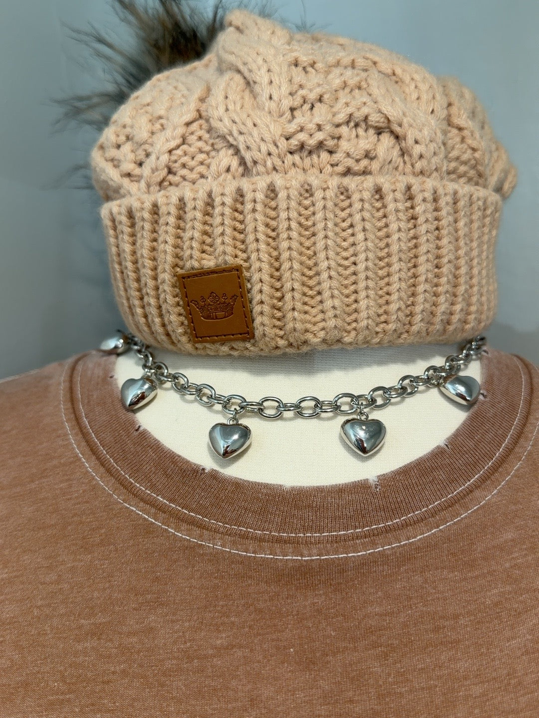 Silver chain necklace with five puffed heart charms displayed with knit hat